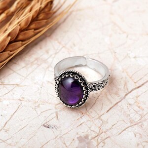 Adjustable oval ring made of 925 sterling silver with a green peridot stone on one side and a purple amethyst stone on the other, showing an oxidized antique finish.