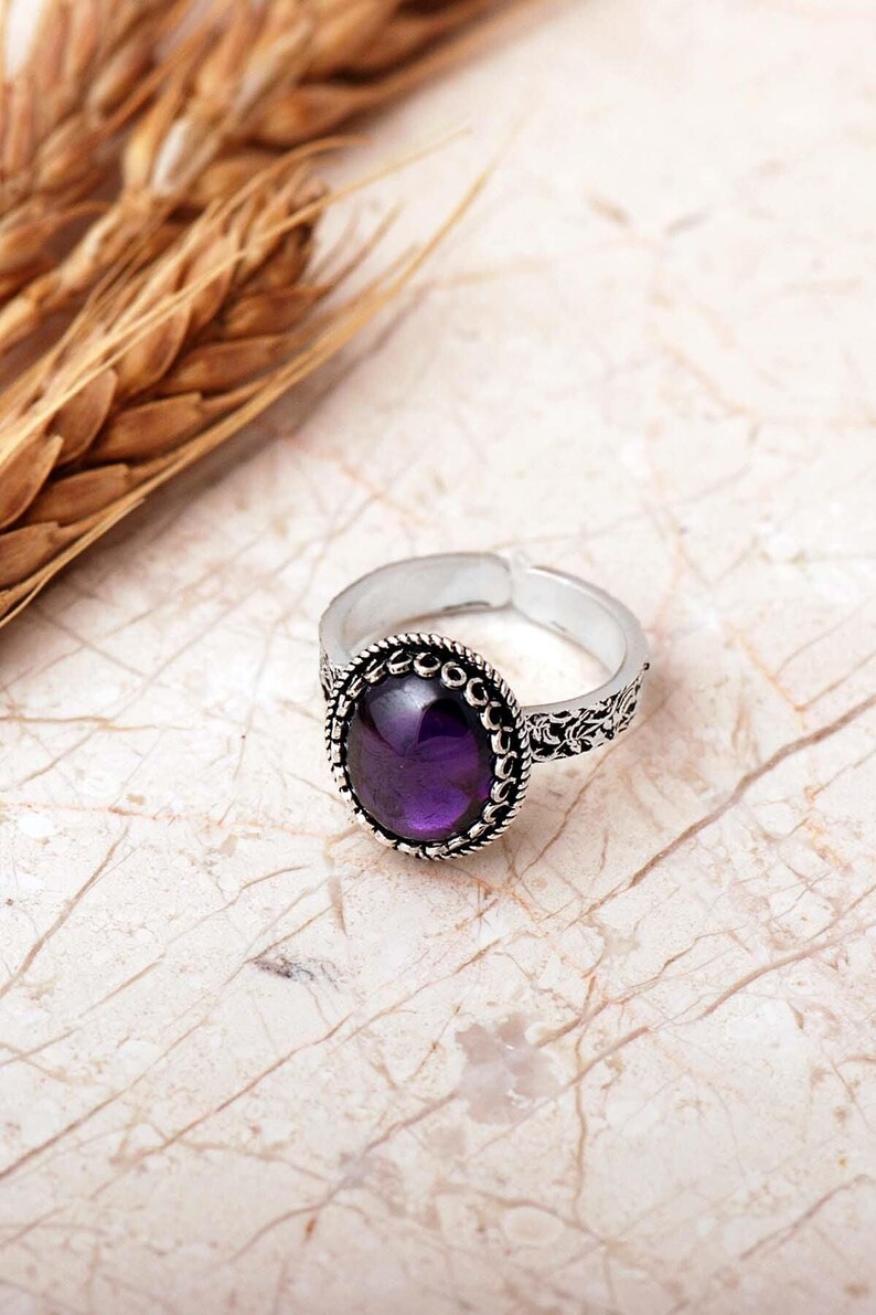 Adjustable oval ring made of 925 sterling silver with a green peridot stone on one side and a purple amethyst stone on the other, showing an oxidized antique finish.