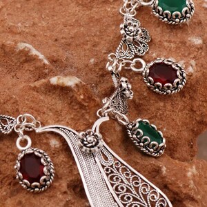 Close-up of silver filigree necklace featuring green and red gemstones