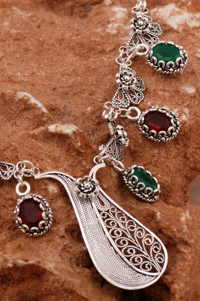 Close-up of silver filigree necklace featuring green and red gemstones