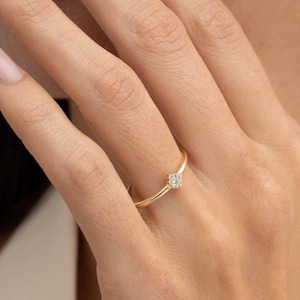 May include: A thin gold band ring featuring a small, square-shaped cluster of tiny, clear, sparkling stones set at the center. The metal has a polished, smooth finish, and the design is simple, showcasing a delicate and slender profile.