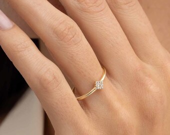 May include: A thin gold band ring featuring a small, square-shaped cluster of tiny, clear, sparkling stones set at the center. The metal has a polished, smooth finish, and the design is simple, showcasing a delicate and slender profile.