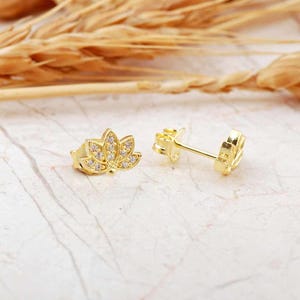 May include: A pair of gold-tone earrings with a lotus flower design. The earrings are adorned with small, clear cubic zirconia stones.