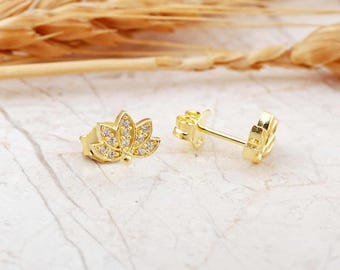 May include: A pair of gold-tone earrings with a lotus flower design. The earrings are adorned with small, clear cubic zirconia stones.