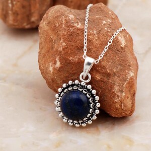 May include: A silver necklace with a round pendant featuring a dark blue lapis lazuli stone surrounded by a silver beaded border.