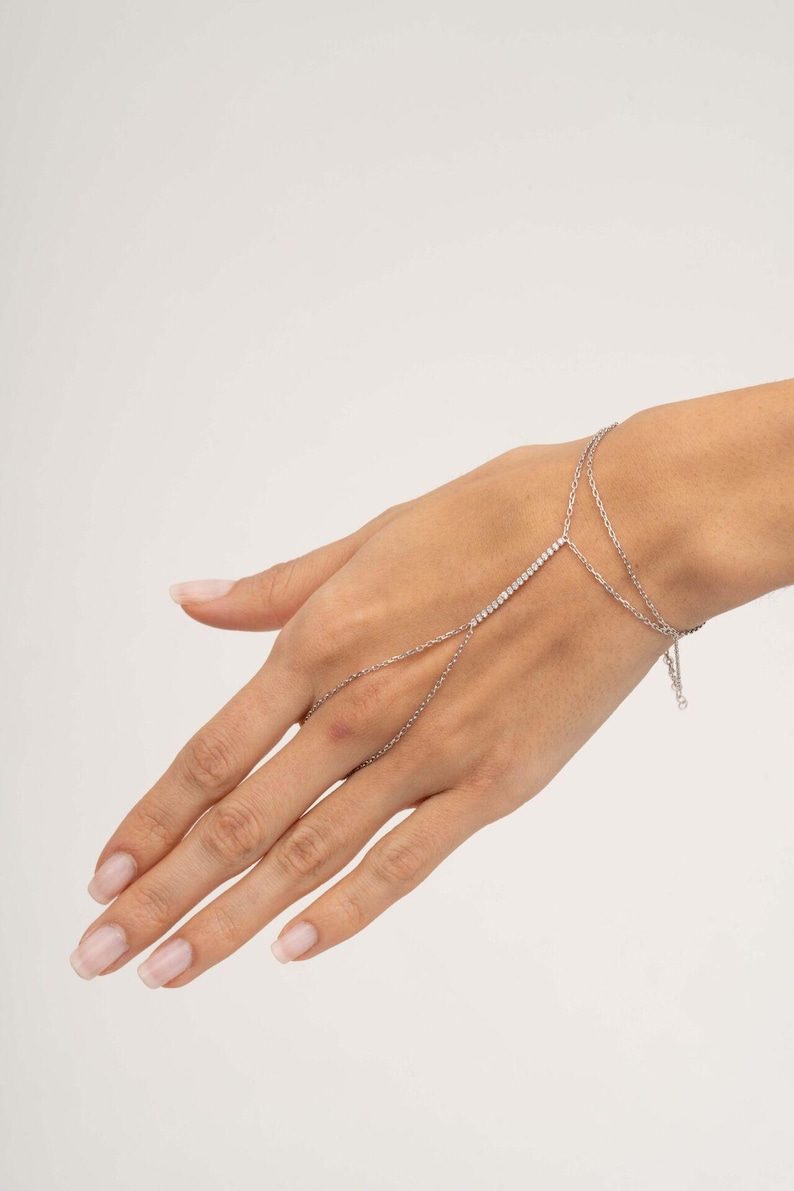 A sparkling 925 sterling silver hand harness bracelet featuring clear cubic zirconia tennis stones that wraps twice around the wrist and connects elegantly to a finger ring.