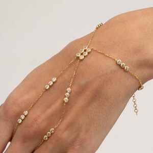 A gold-plated 925 sterling silver hand harness bracelet featuring delicate chains connecting a finger ring to a wrist bracelet embellished with sparkling round clear zircon gemstones.