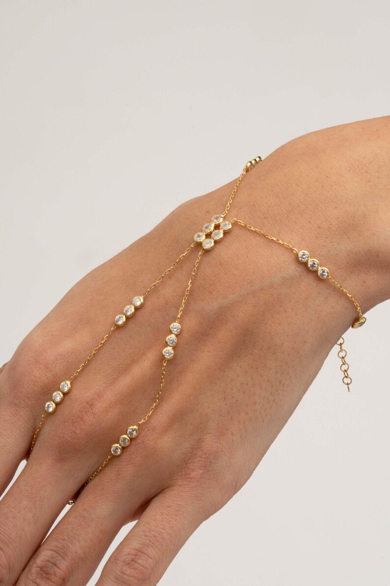 A gold-plated 925 sterling silver hand harness bracelet featuring delicate chains connecting a finger ring to a wrist bracelet embellished with sparkling round clear zircon gemstones.