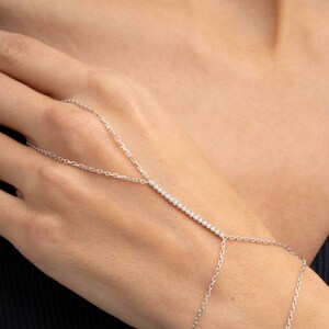 A sparkling 925 sterling silver hand harness bracelet featuring clear cubic zirconia tennis stones that wraps twice around the wrist and connects elegantly to a finger ring.