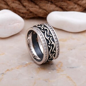Handmade 925 sterling silver women's 9 mm wide wedding band adorned with sparkling cubic zirconia stones and finished in shiny white rhodium plating.