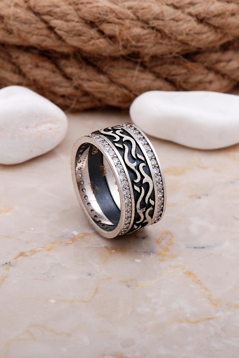 Handmade 925 sterling silver women's 9 mm wide wedding band adorned with sparkling cubic zirconia stones and finished in shiny white rhodium plating.