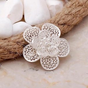 May include: A silver filigree flower brooch with a delicate, intricate design. The flower has five petals and a center with small, round beads.