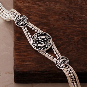 A handcrafted 925 sterling silver woven mesh bracelet featuring circular silver medallions decorated with black enamel tulip motifs and an adjustable lobster claw clasp.