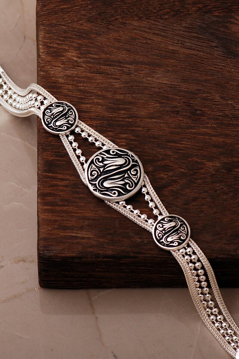 A handcrafted 925 sterling silver woven mesh bracelet featuring circular silver medallions decorated with black enamel tulip motifs and an adjustable lobster claw clasp.