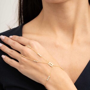 A gold-plated 925 sterling silver hand harness bracelet featuring delicate chains connecting a finger ring to a wrist bracelet embellished with sparkling round clear zircon gemstones.