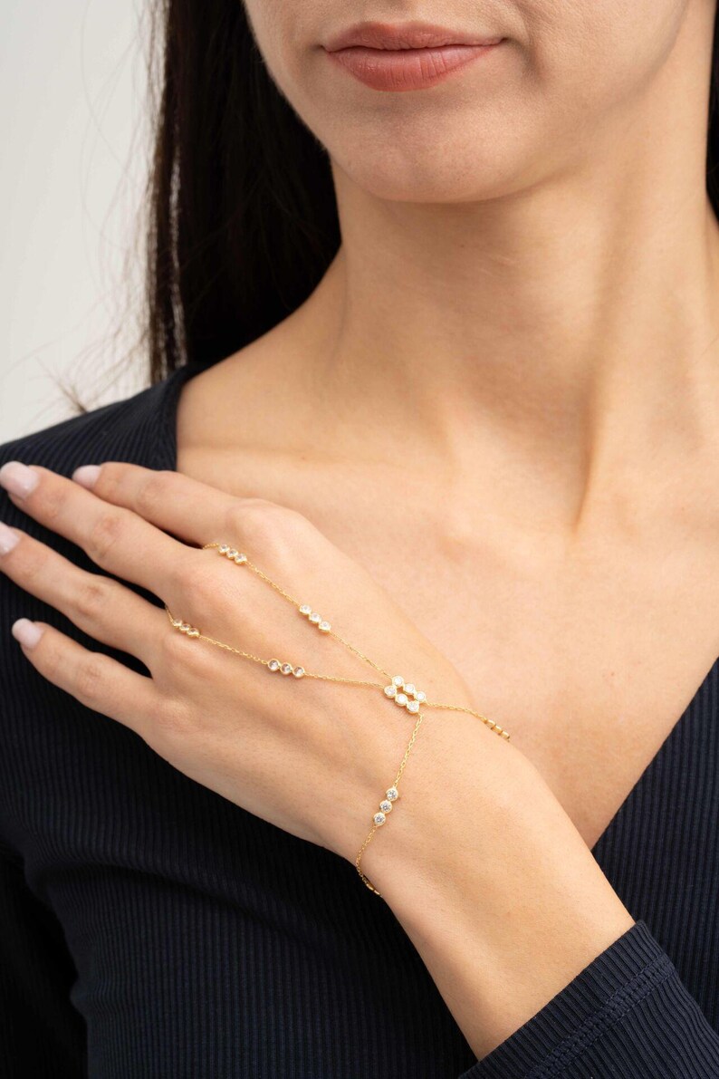 A gold-plated 925 sterling silver hand harness bracelet featuring delicate chains connecting a finger ring to a wrist bracelet embellished with sparkling round clear zircon gemstones.