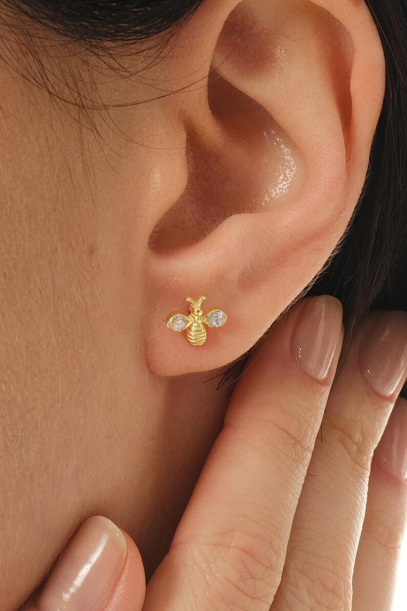 A pair of small 925 sterling silver earrings shaped like bees, coated in gold‑rhodium and set with white zircon stones, measuring 7 mm in length.
