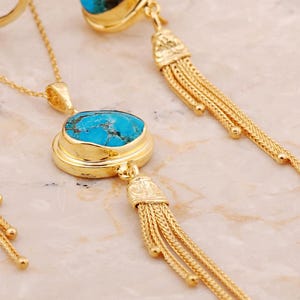 A handmade 925 sterling silver gold plated jewelry set featuring a woven tassel pendant necklace, dangling earrings, and an adjustable ring, all adorned with natural blue turquoise stones.