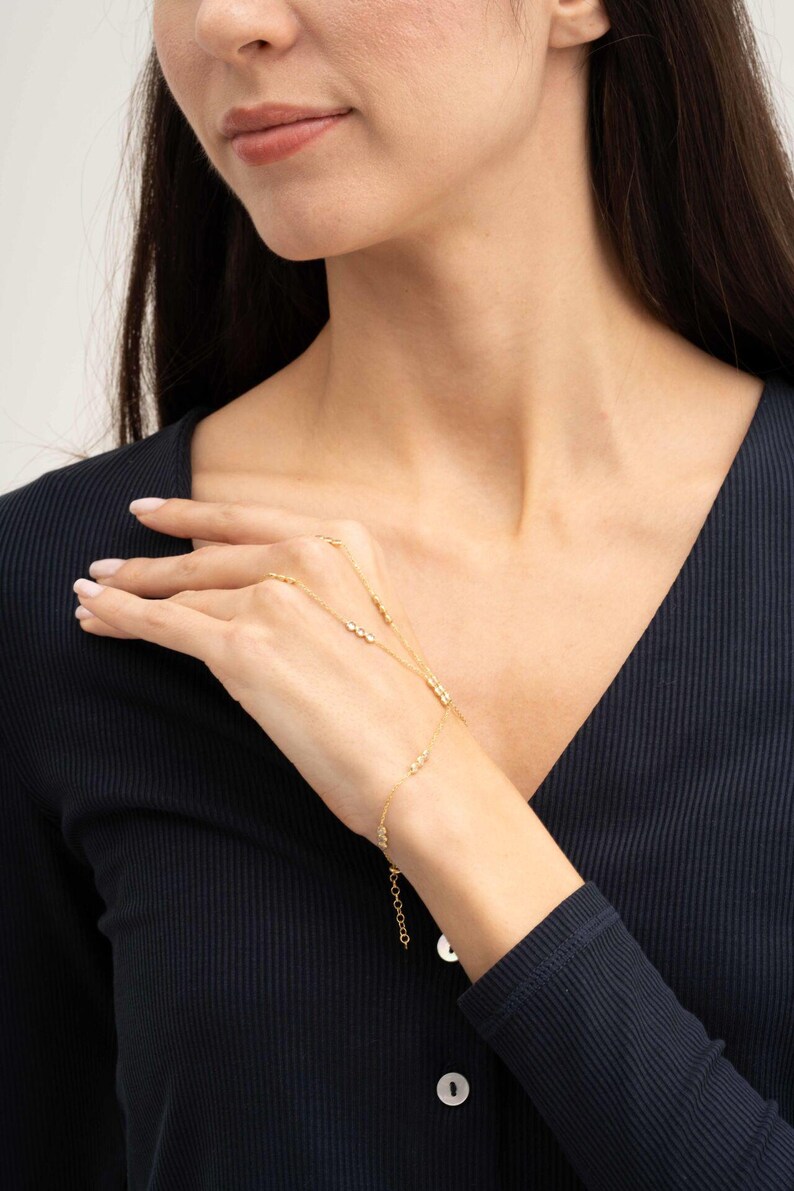 A gold-plated 925 sterling silver hand harness bracelet featuring delicate chains connecting a finger ring to a wrist bracelet embellished with sparkling round clear zircon gemstones.