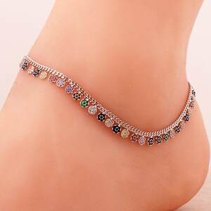 May include: A silver-toned metal anklet featuring a delicate curb chain adorned with a series of small, circular charms. Each charm is encrusted with tiny, multi-colored gemstones in shades of blue, green, yellow, pink, and clear white.