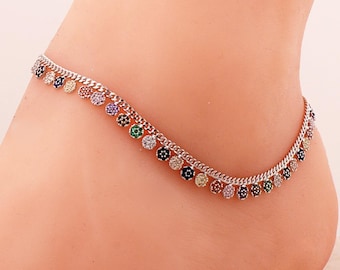 May include: A silver-toned metal anklet featuring a delicate curb chain adorned with a series of small, circular charms. Each charm is encrusted with tiny, multi-coloured gemstones in shades of blue, green, yellow, pink, and clear white.