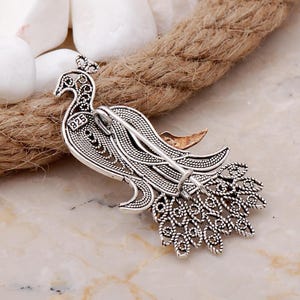 A handmade 925 sterling silver filigree brooch shaped like a peacock, featuring gold-toned accents and set with root ruby and emerald stones.