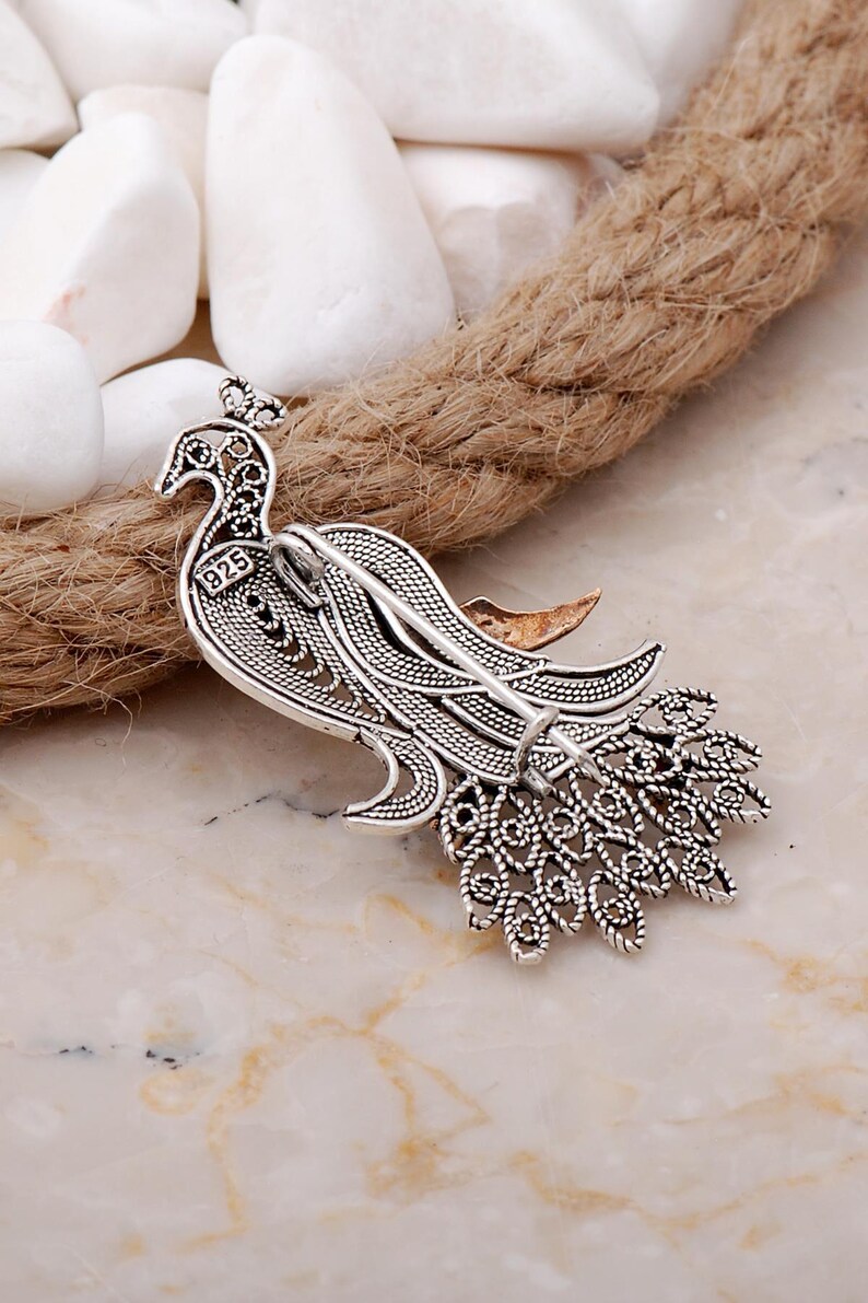 A handmade 925 sterling silver filigree brooch shaped like a peacock, featuring gold-toned accents and set with root ruby and emerald stones.