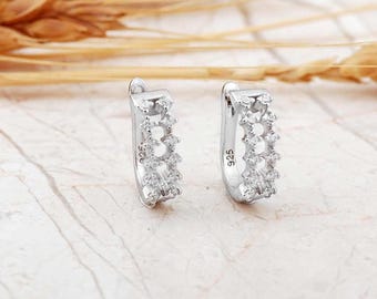 May include: A pair of silver hoop earrings featuring a double row of small clear stones set along the front edge. Each earring is stamped with 925 on the inner side, indicating sterling silver construction. The hoops have a hinged closure.