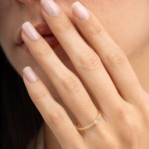 A close‑up of a thin silver ring with green gold plating and sparkling zircon stones, featuring a larger 2.5 mm center stone and smaller 1.5 mm accents.
