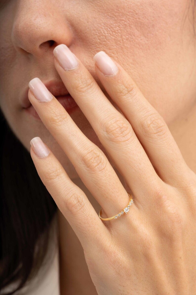 A close‑up of a thin silver ring with green gold plating and sparkling zircon stones, featuring a larger 2.5 mm center stone and smaller 1.5 mm accents.