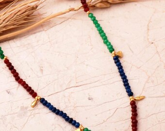 May include: A beaded necklace featuring faceted beads in alternating segments of blue, red, and green. The necklace is accented with small gold-toned metal charms shaped like leaves and triangles, spaced evenly along the strand of colorful beads.