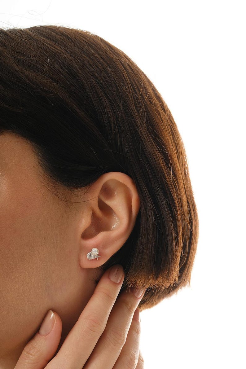 A pair of mini 925 sterling silver stud earrings featuring a detailed seashell and starfish motif accented with a small white pearl and butterfly backs.