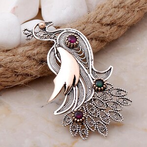 A handmade 925 sterling silver filigree brooch shaped like a peacock, featuring gold-toned accents and set with root ruby and emerald stones.