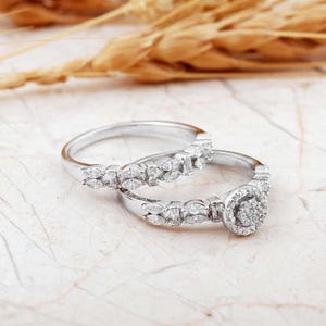 May include: A set of two silver-toned rings featuring marquise-cut stones along the bands. One ring includes a central circular cluster of small round stones, while the other band is adorned with a continuous row of marquise-cut stones.