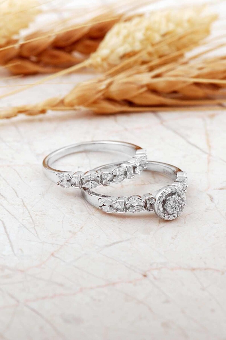 A pair of white rhodium‑plated sterling silver rings; the larger solitaire features a clear zircon stone, and the slimmer band complements it with a sleek design.