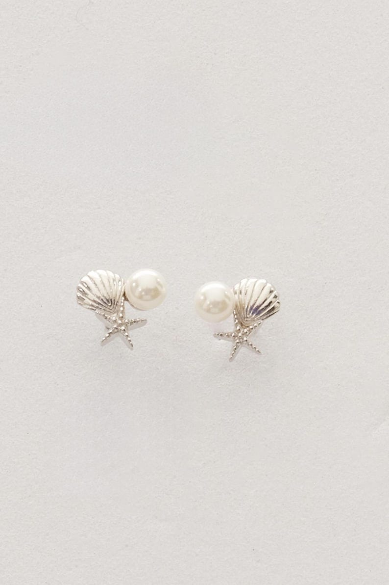 A pair of mini 925 sterling silver stud earrings featuring a detailed seashell and starfish motif accented with a small white pearl and butterfly backs.