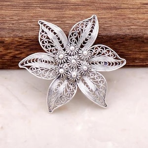 May include: A silver filigree flower brooch with a detailed design and a cluster of small round beads in the center.