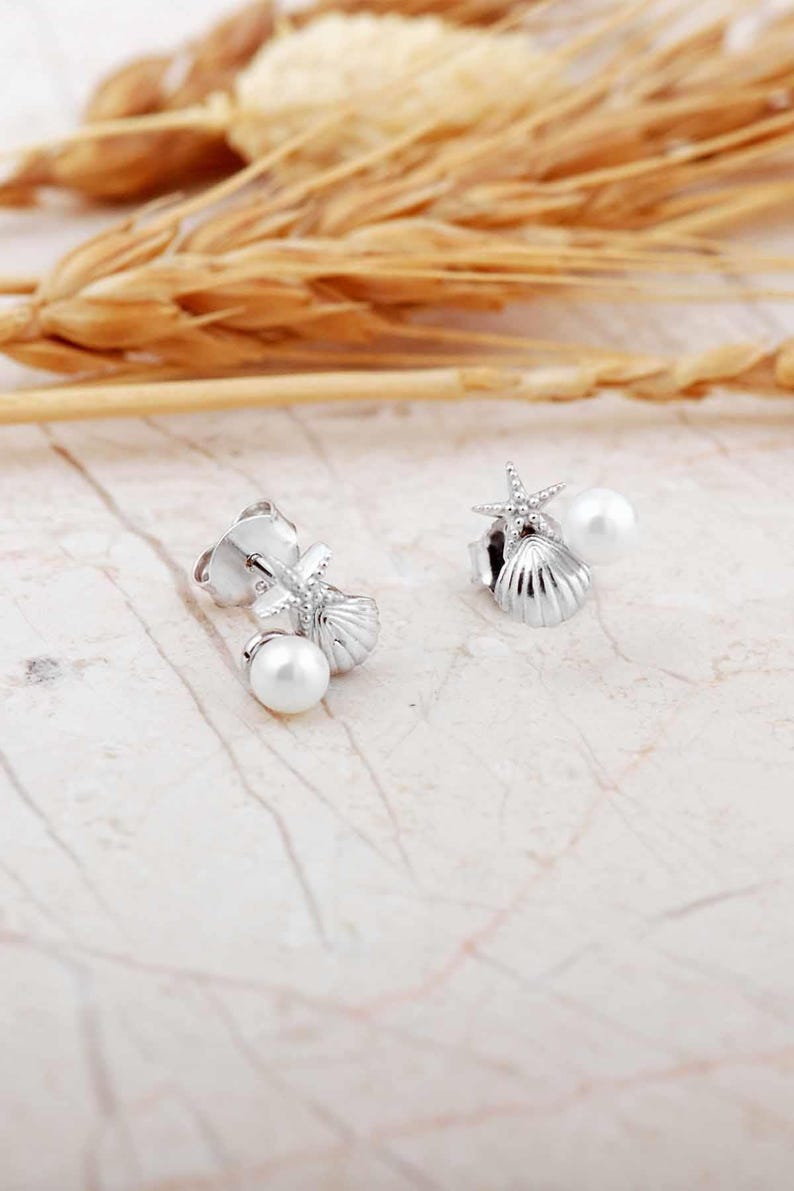 A pair of mini 925 sterling silver stud earrings featuring a detailed seashell and starfish motif accented with a small white pearl and butterfly backs.