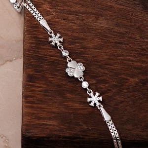A delicate 925 sterling silver box chain bracelet featuring a four-leaf clover and snowflake charm set with clear cubic zirconia stones.