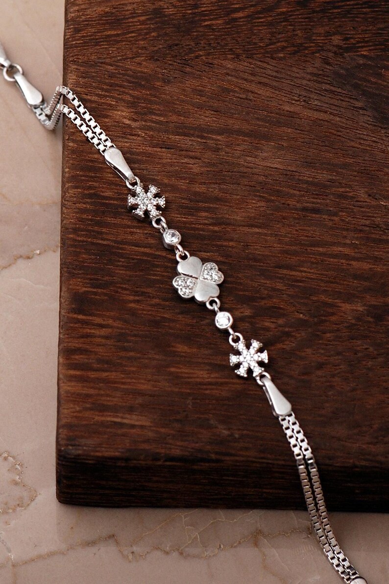 A delicate 925 sterling silver box chain bracelet featuring a four-leaf clover and snowflake charm set with clear cubic zirconia stones.