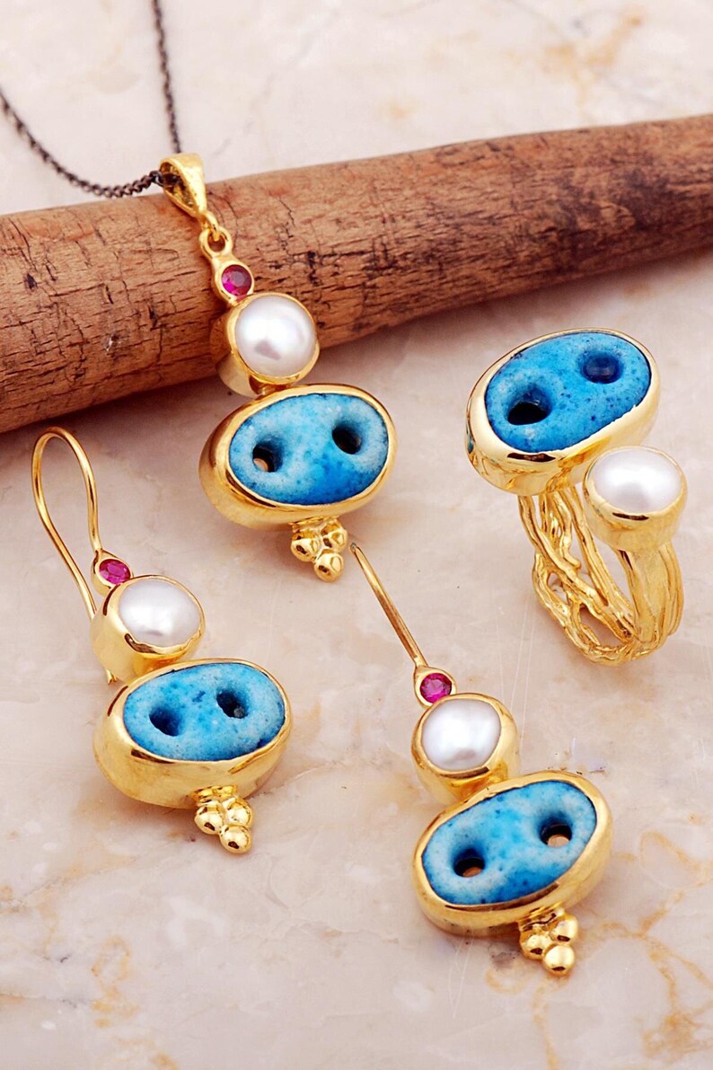 A handmade 925 sterling silver jewelry set with gold plating, featuring a pendant necklace, drop earrings, and an adjustable ring embellished with Syriac turquoise evil eye stones, pearls, and ruby accents.
