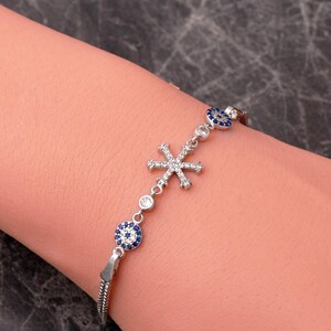 A delicate 925 sterling silver bracelet featuring a sparkling snowflake design combined with a blue sapphire and cubic zirconia evil eye charm on an adjustable box chain.