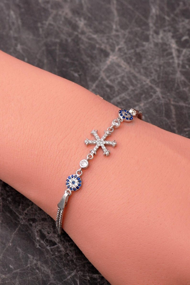 A delicate 925 sterling silver bracelet featuring a sparkling snowflake design combined with a blue sapphire and cubic zirconia evil eye charm on an adjustable box chain.