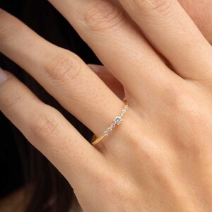 A close‑up of a thin silver ring with green gold plating and sparkling zircon stones, featuring a larger 2.5 mm center stone and smaller 1.5 mm accents.