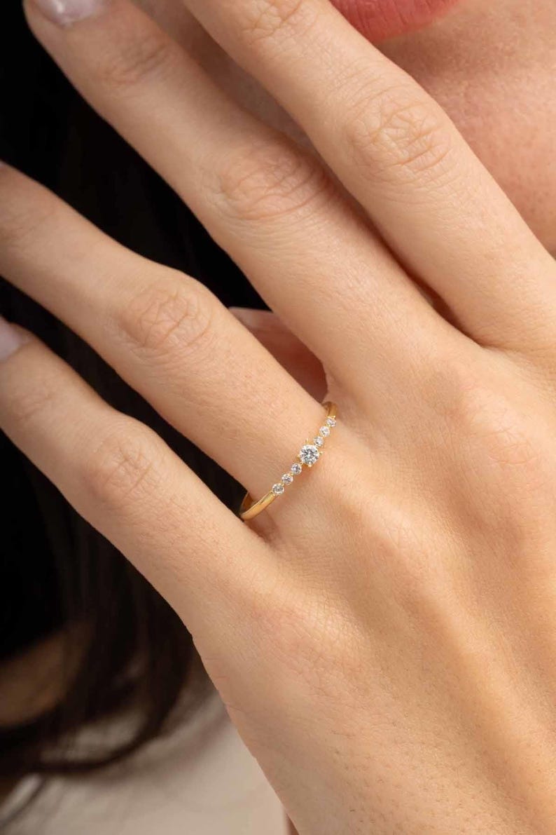 A close‑up of a thin silver ring with green gold plating and sparkling zircon stones, featuring a larger 2.5 mm center stone and smaller 1.5 mm accents.