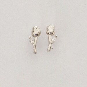 A pair of small silver earrings featuring a minimalist tulip shape adorned with sparkling white zircon stones, rhodium‑plated for a bright finish.