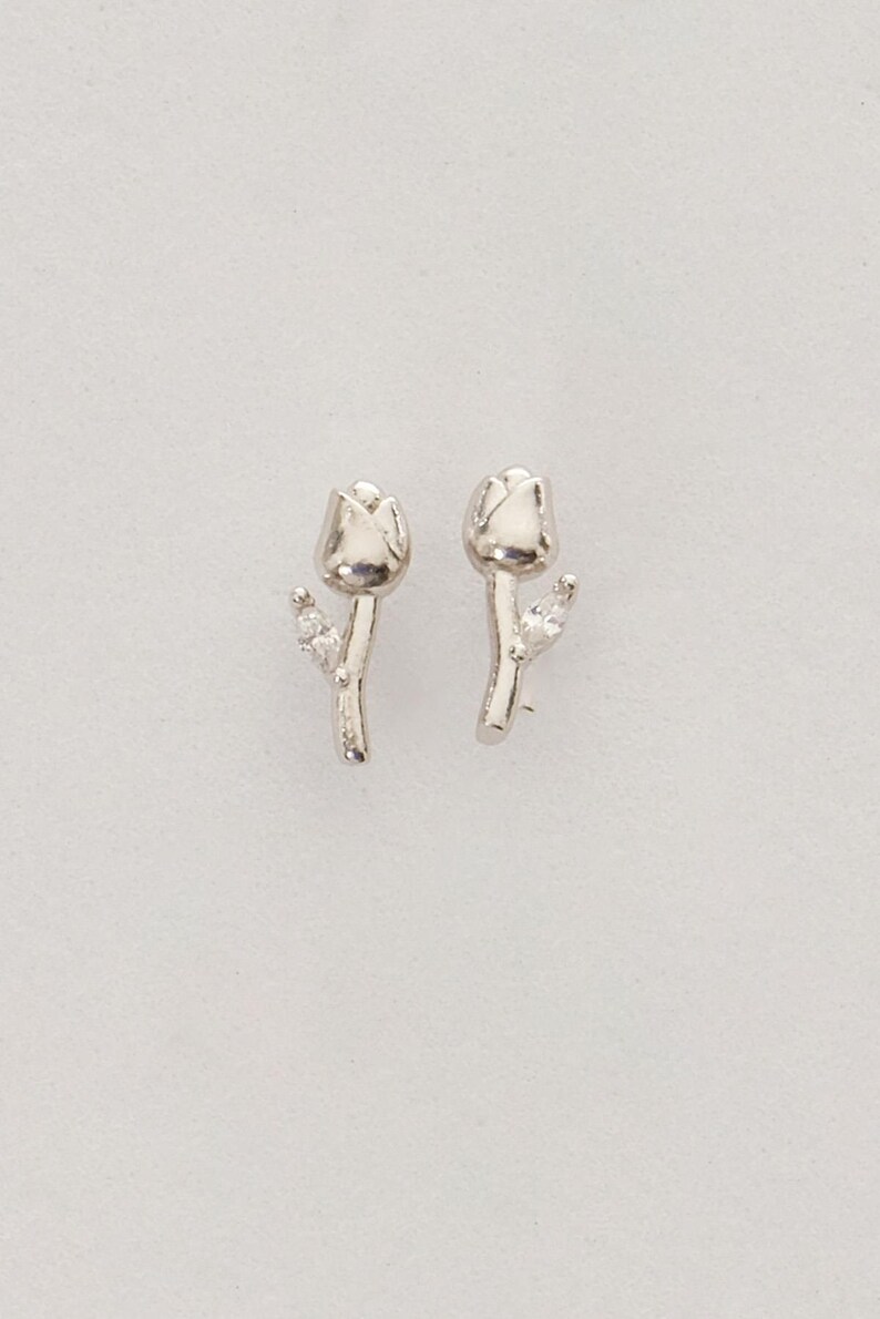 A pair of small silver earrings featuring a minimalist tulip shape adorned with sparkling white zircon stones, rhodium‑plated for a bright finish.