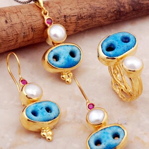A handmade 925 sterling silver jewelry set with gold plating, featuring a pendant necklace, drop earrings, and an adjustable ring embellished with Syriac turquoise evil eye stones, pearls, and ruby accents.