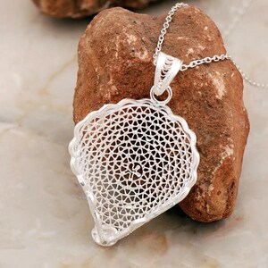 May include: A silver filigree pendant necklace with a delicate, intricate design. The pendant is shaped like a shell and has a circular pattern in the center. The necklace is on a silver chain.