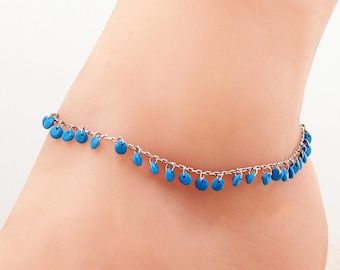 May include: A silver-toned metal anklet featuring a delicate chain adorned with numerous small, round, bright turquoise-blue charms hanging at regular intervals along the entire length of the chain.